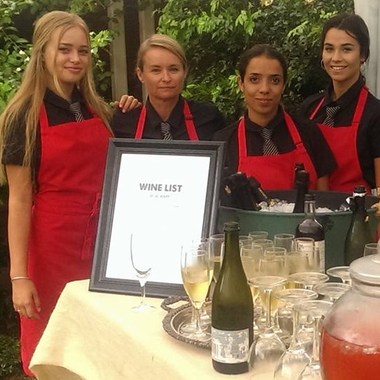 Four waitresses dressed in black with red aprons at the wine bar