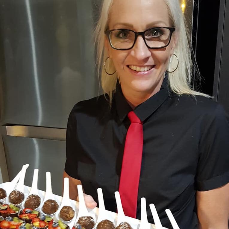 Smiling waitress with glasses in black with red tie holding a platter of desserts