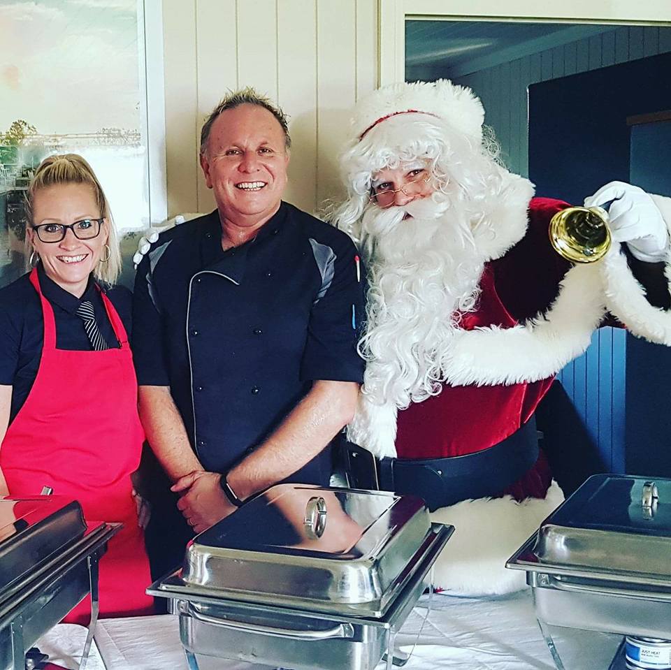 Waitress, Chef and Santa claus smiling in front of buffet